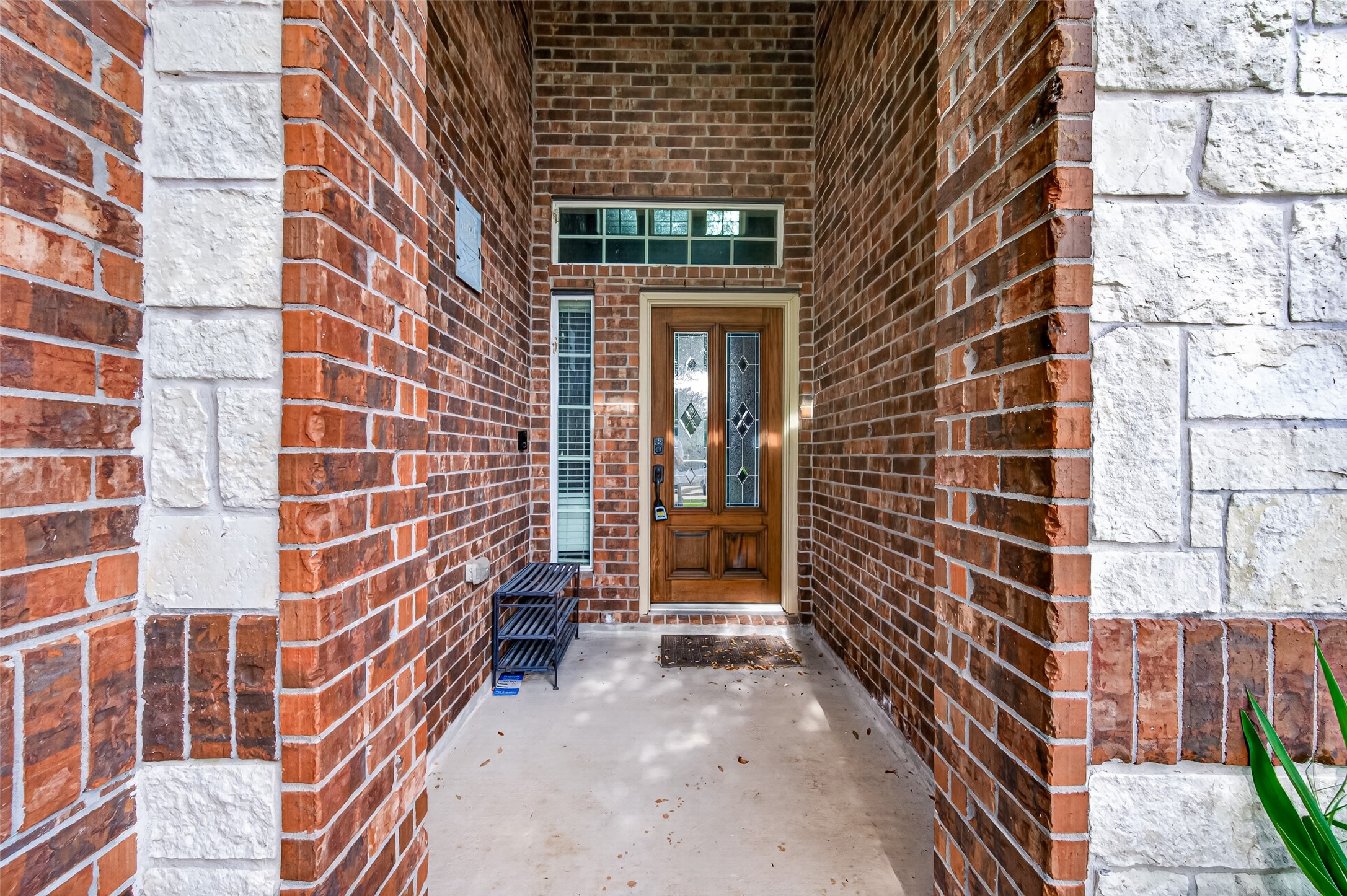 Covered brick and stone entry with decorative glass front door, sidelight and transom window.