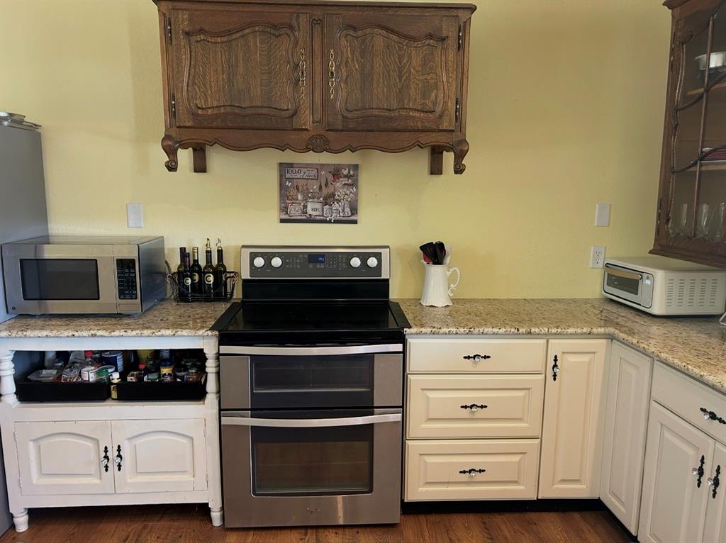 1794 Cr 527 Road Baird, TX 79504 - Photo 20 of 38 Granite-finish countertops, dual wall cabinetry with decorative hardware, stainless steel electric range with double ovens, and wood-finish flooring