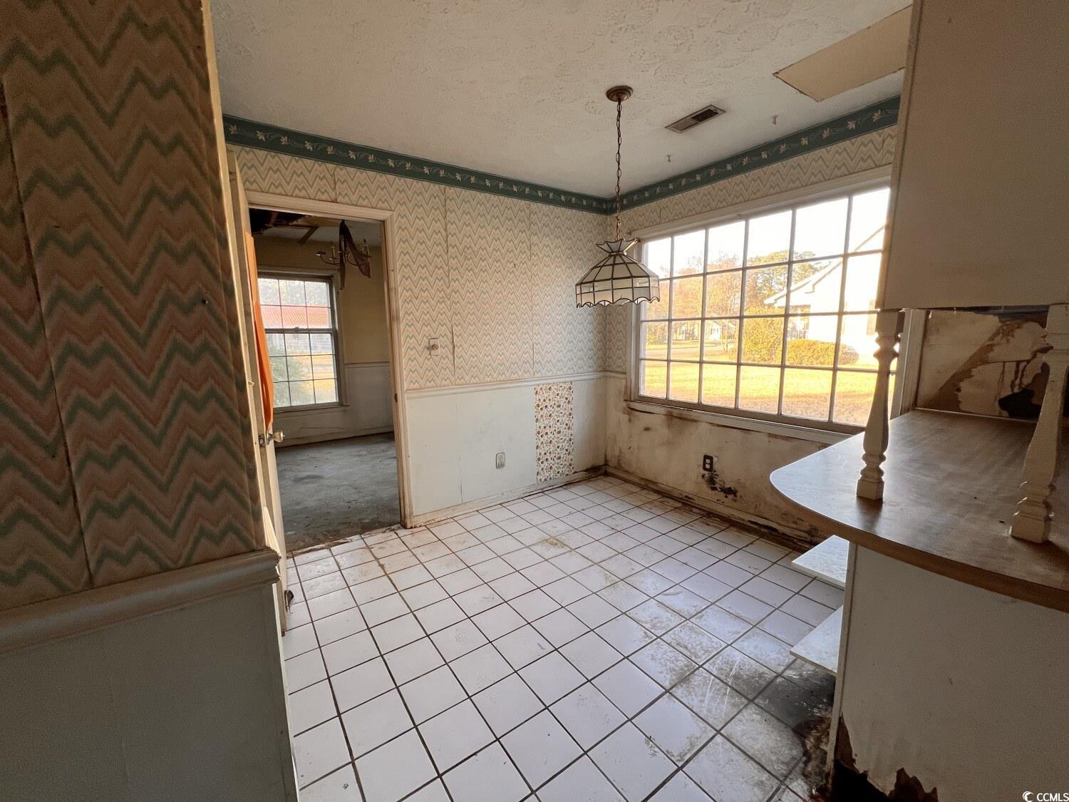 33 Plantation Road Myrtle Beach, SC 29588 - Photo 6 of 22 Unfurnished dining area with wallpapered walls, a textured ceiling, healthy amount of natural light, wainscoting, and light tile patterned floors
