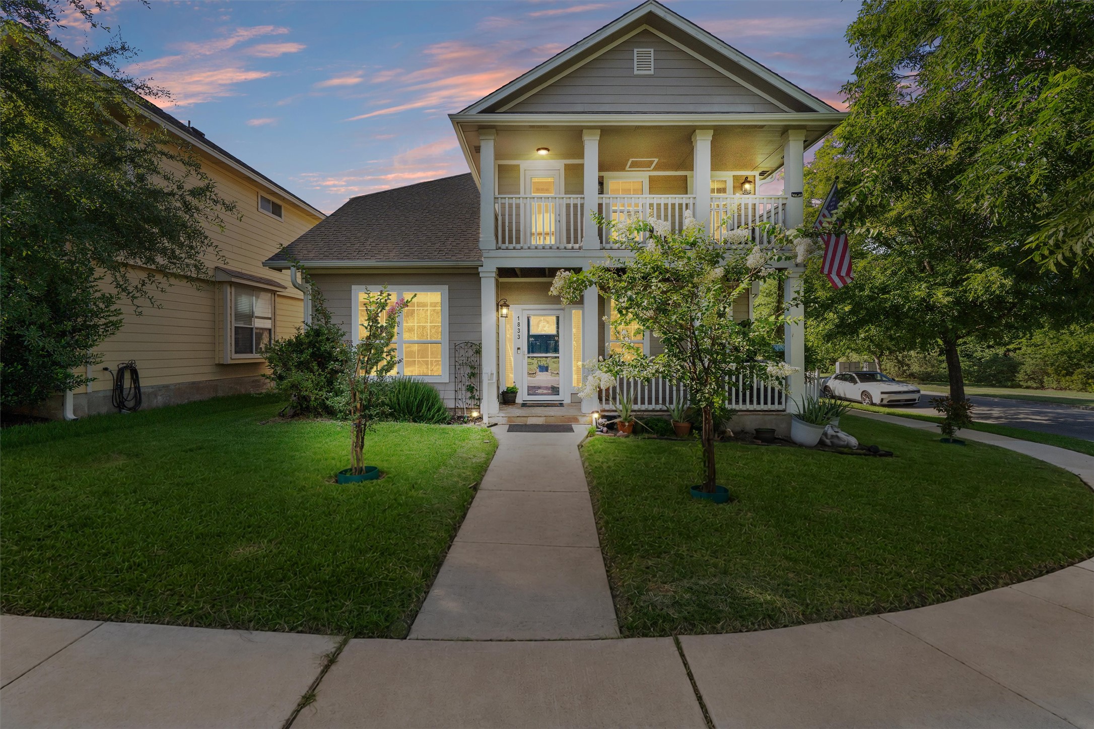 A charming two-story home with a welcoming front porch and upper-level balcony, nestled among mature trees.