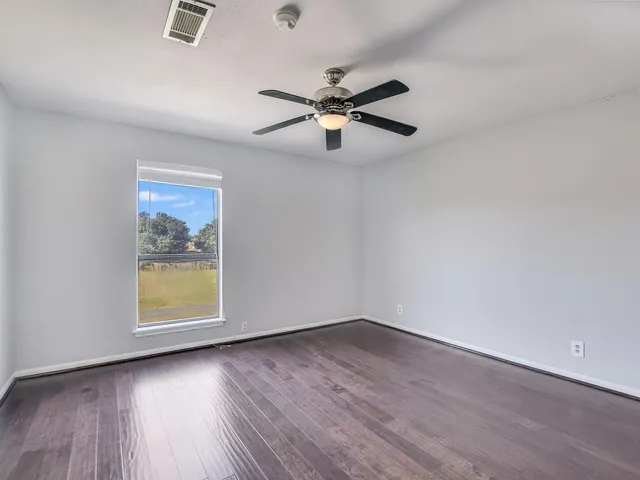 an empty room with wooden floor chandelier fan and windows