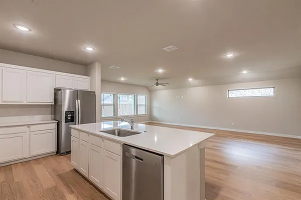 a kitchen with stainless steel appliances granite countertop a sink dishwasher a refrigerator and white cabinets with wooden floor
