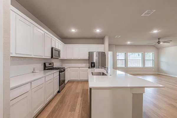 a kitchen with stainless steel appliances granite countertop a sink dishwasher a stove and white cabinets with wooden floor