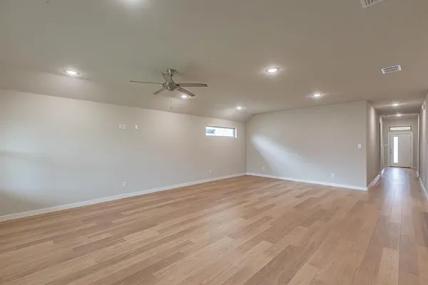 a view of an empty room with wooden floor and a ceiling fan