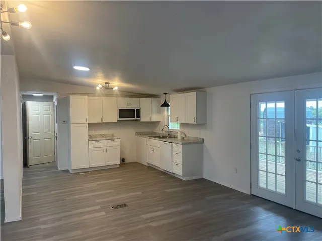 a large white kitchen with wooden floor and stainless steel appliances