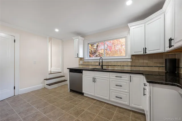 a kitchen with granite countertop a sink white cabinets and a dishwasher next to a window