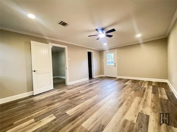 a view of an empty room with wooden floor and a ceiling fan