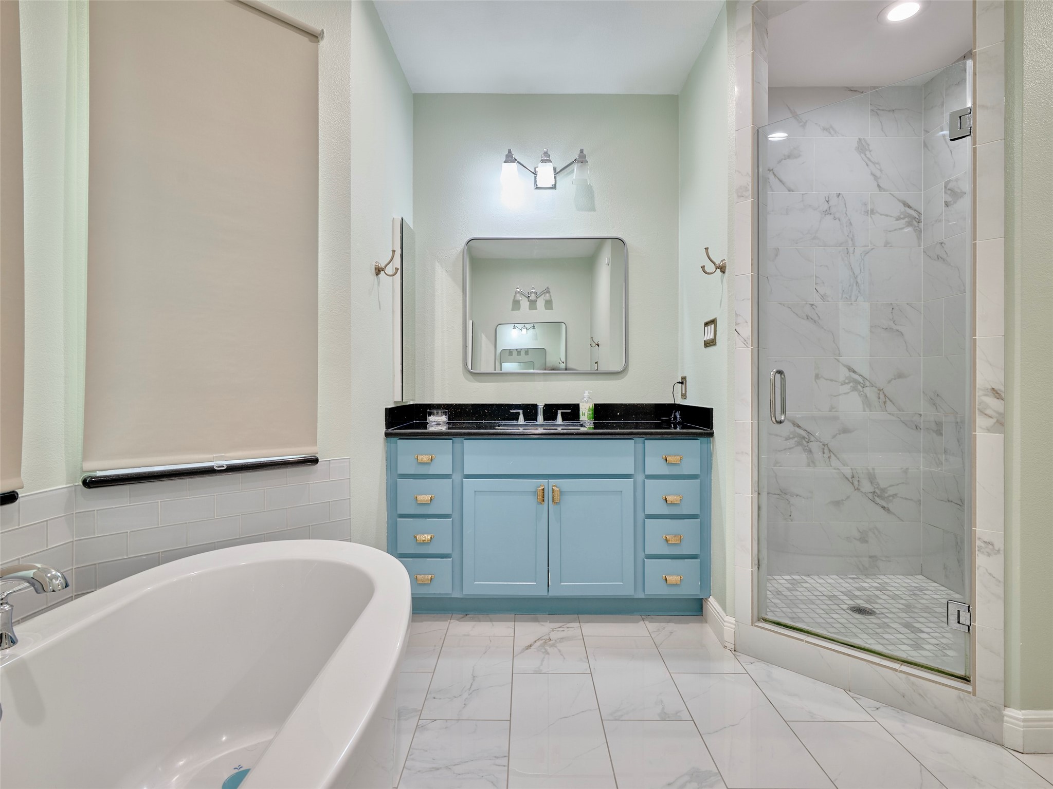 4219 Redbud Street Houston, TX 77051 - Photo 19 of 25 This bathroom features a sleek design with a large soaking tub, a spacious glass-enclosed shower with marble tile, and a vanity with blue cabinetry and black countertop. The room is well-lit and has modern fixtures, offering a fresh and inviting atmosphere.