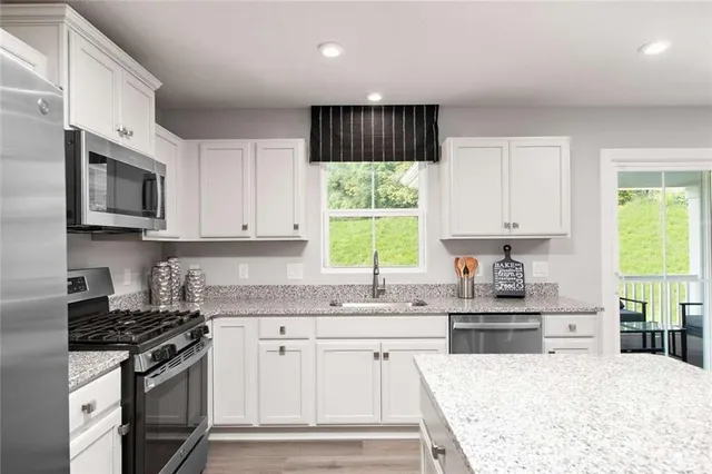 a kitchen with stainless steel appliances granite countertop a stove a sink dishwasher and a microwave oven with white cabinets