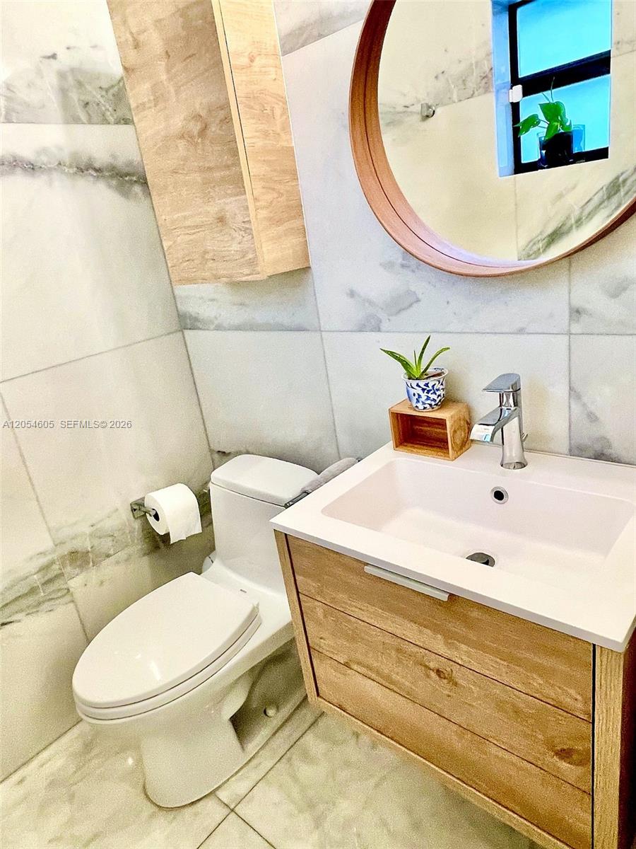 3538 Southwest 1st Avenue, Unit 1 Miami, FL 33145 - Photo 16 of 20 Stylish half bathroom featuring marble-style finishes, a floating wood vanity with a modern rectangular sink, coordinating wall-mounted storage, and a round wood-framed mirror. Natural light, clean lines, and warm wood accents create a bright and welcoming space for guests