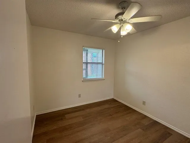 an empty room with a chandelier fan and wooden floor