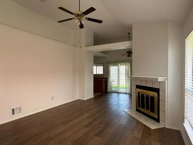 an empty room with wooden floor a ceiling fan a fireplace and windows