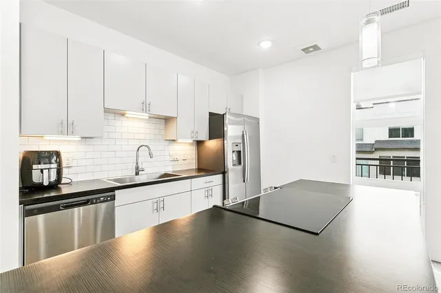 a kitchen with stainless steel appliances a sink dishwasher a refrigerator a stove and white cabinets with wooden floor