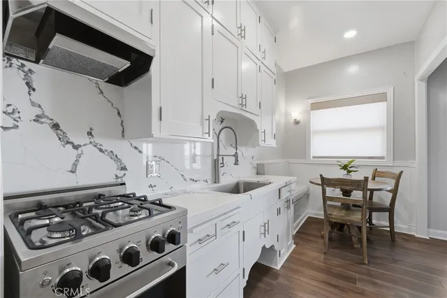 a kitchen with stainless steel appliances a stove a sink dishwasher and white cabinets with wooden floor