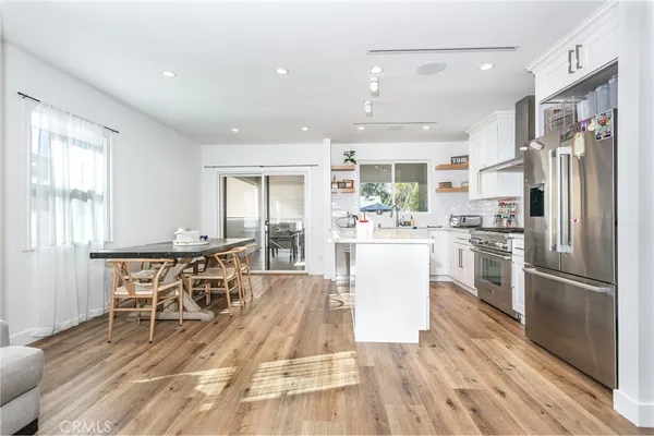 a kitchen with stainless steel appliances kitchen island granite countertop a refrigerator a stove a dining table and chairs with wooden floor