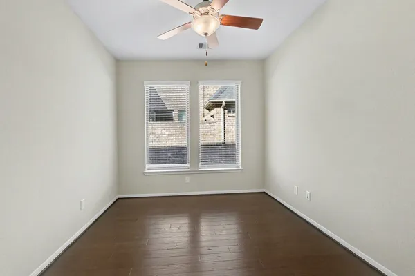 an empty room with wooden floor chandelier fan and windows