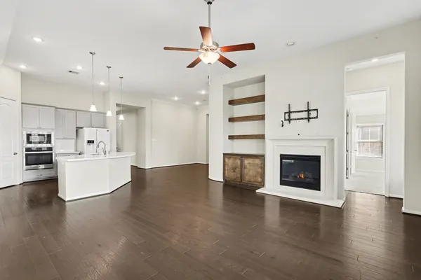 a view of an empty room and kitchen with fireplace wooden floor
