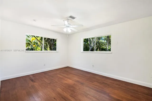 an empty room with wooden floor ceiling fan and windows