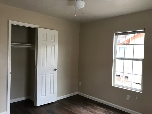 an empty room with wooden floor closet and windows