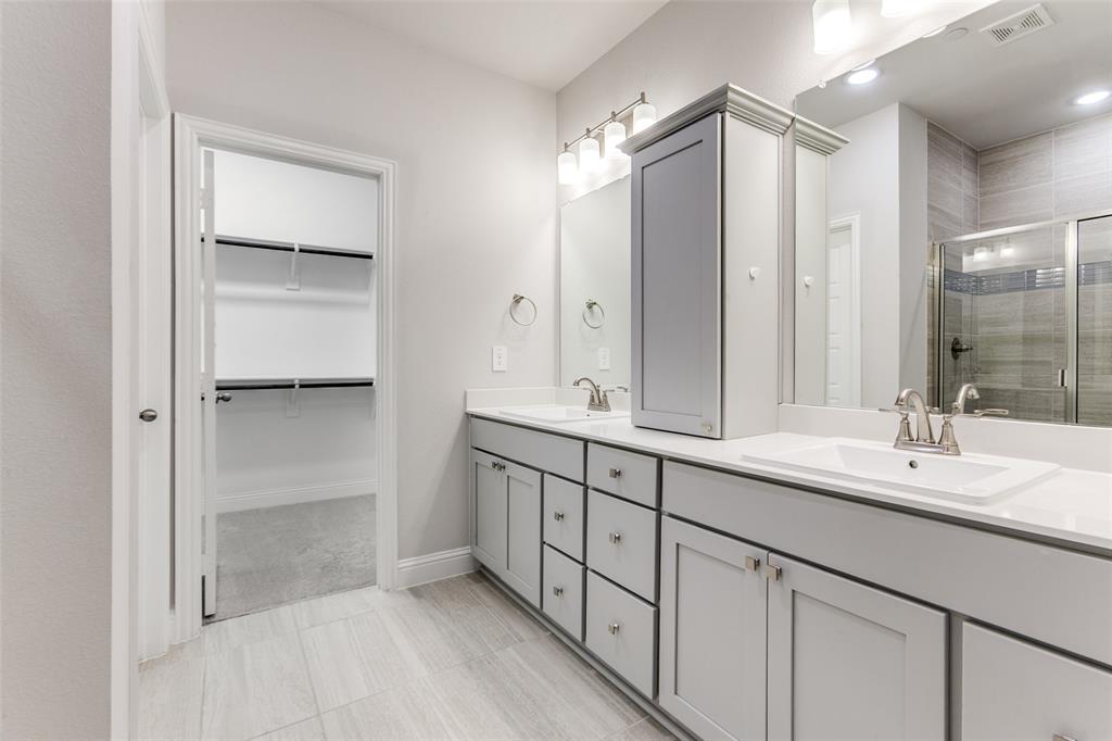 1888 Strand Street Dallas, TX 75234 - Photo 9 of 13 Bathroom featuring dual vanities with white countertops, light gray cabinetry with brushed nickel hardware, and a glass-enclosed shower with tile surround