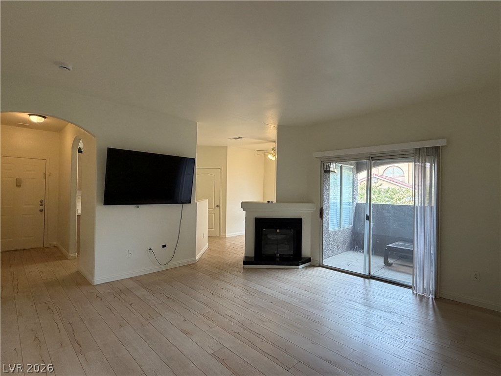 5525 West Flamingo Road, Unit 2016 Las Vegas, NV 89103 - Photo 13 of 20 Unfurnished living room featuring arched walkways, light wood-style flooring, a glass covered fireplace, and a ceiling fan
