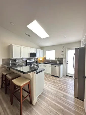 a kitchen with stainless steel appliances a stove a sink dishwasher a refrigerator and white cabinets with wooden floor