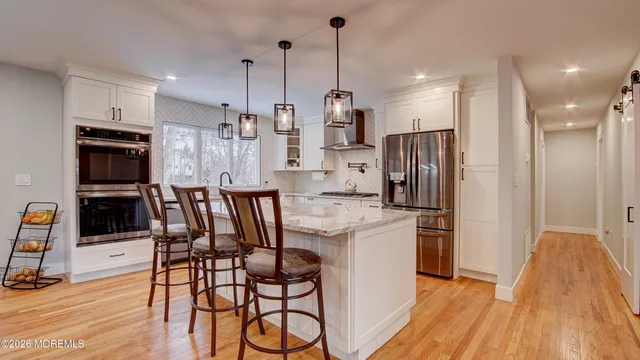 a kitchen with stainless steel appliances kitchen island granite countertop a refrigerator a stove a microwave oven a sink with island and chairs with wooden floor