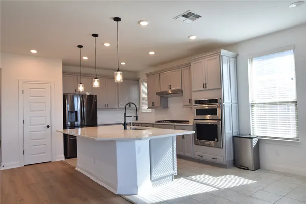 a large kitchen with stainless steel appliances kitchen island granite countertop a refrigerator a sink and a stove with wooden floor