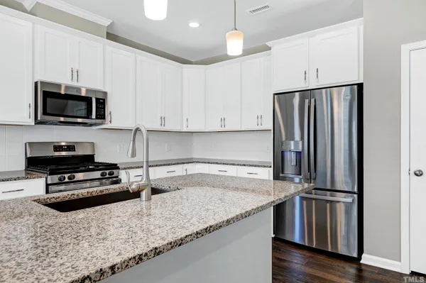 a kitchen with granite countertop a refrigerator a sink a stove a microwave and wooden floor