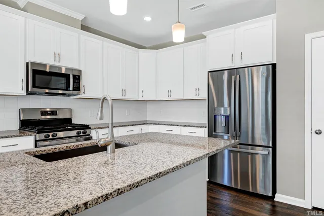 a kitchen with granite countertop a refrigerator a sink a stove a microwave and wooden floor