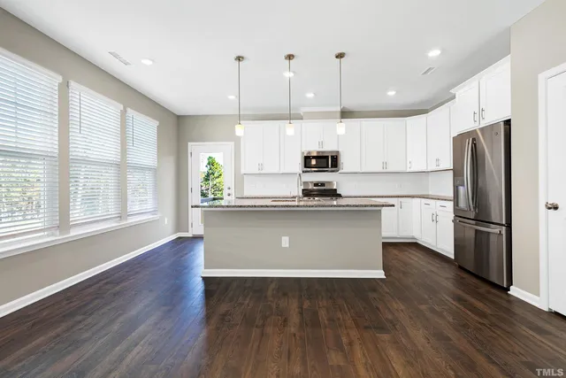 a kitchen with stainless steel appliances a refrigerator a sink cabinets wooden floor and a window