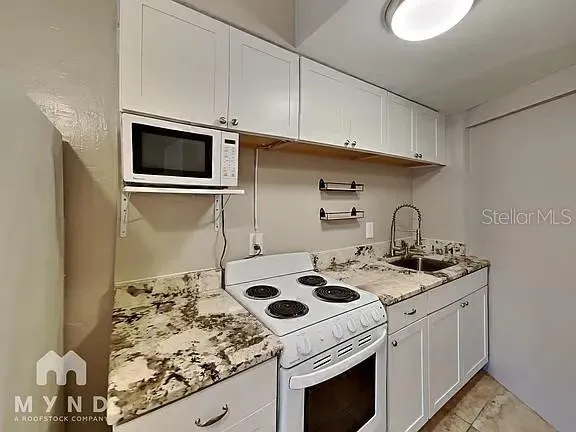 a kitchen with stainless steel appliances granite countertop a refrigerator a sink a stove a microwave oven with white cabinets and wooden floor
