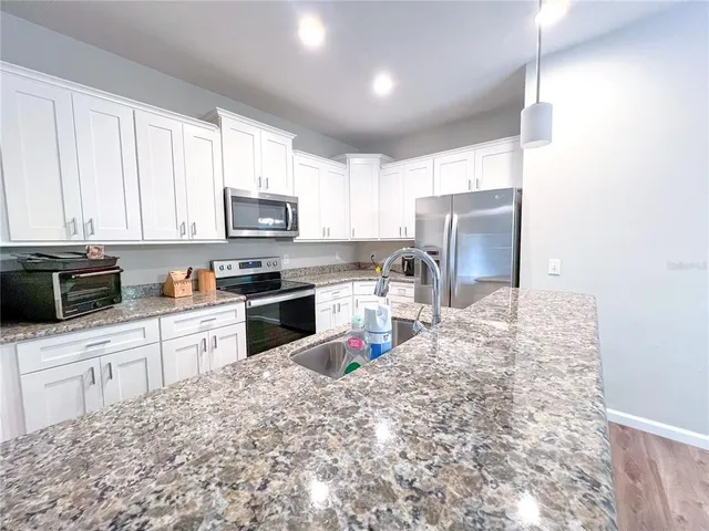 a kitchen with granite countertop a refrigerator sink stove and microwave