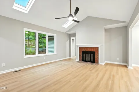 a view of an empty room with wooden floor fireplace and a window