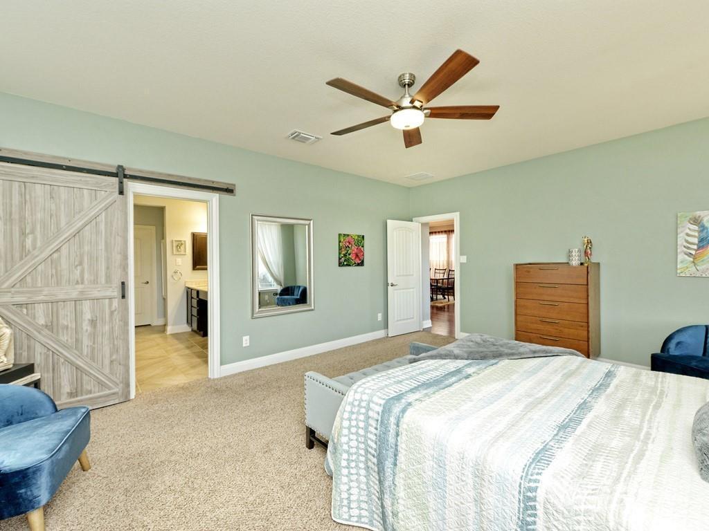 1067 Toltec Trail Georgetown, TX 78626 - Photo 13 of 30 Bedroom with a barn door, a ceiling fan, carpet flooring, and ensuite bath