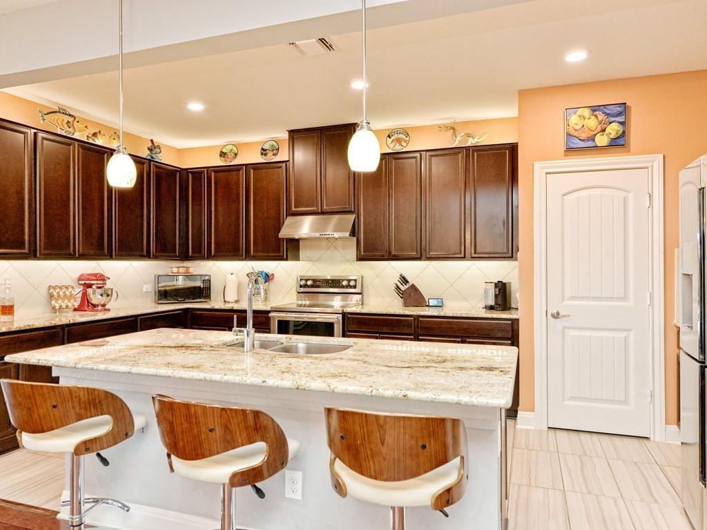 1067 Toltec Trail Georgetown, TX 78626 - Photo 5 of 30 Kitchen featuring dark brown cabinets, decorative light fixtures, a breakfast bar, light stone counters, and recessed lighting