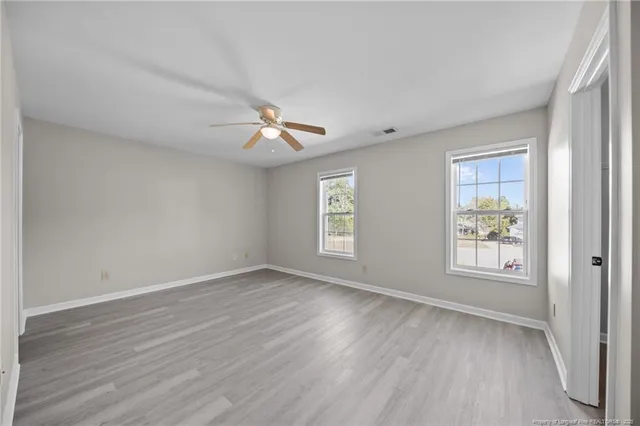 an empty room with wooden floor chandelier fan and windows