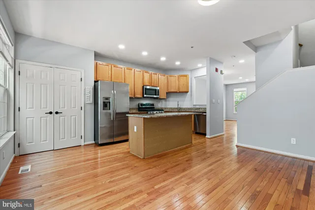 a kitchen with stainless steel appliances granite countertop a stove top oven a sink dishwasher a refrigerator and white cabinets with wooden floor
