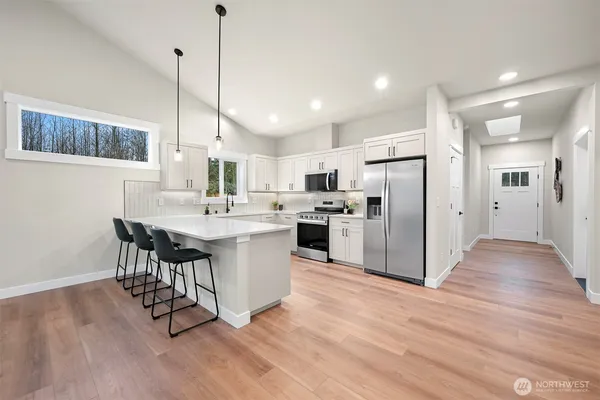 a kitchen with stainless steel appliances a refrigerator a sink dishwasher a stove and white cabinets with wooden floor