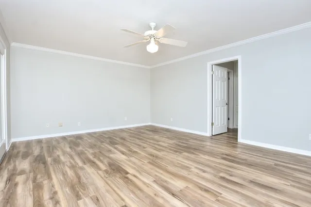 an empty room with wooden floor fan and windows