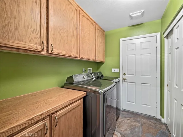 a utility room with stainless steel appliances granite countertop a sink a washer and dryer with wooden cabinets