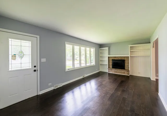 an empty room with wooden floor fireplace and windows