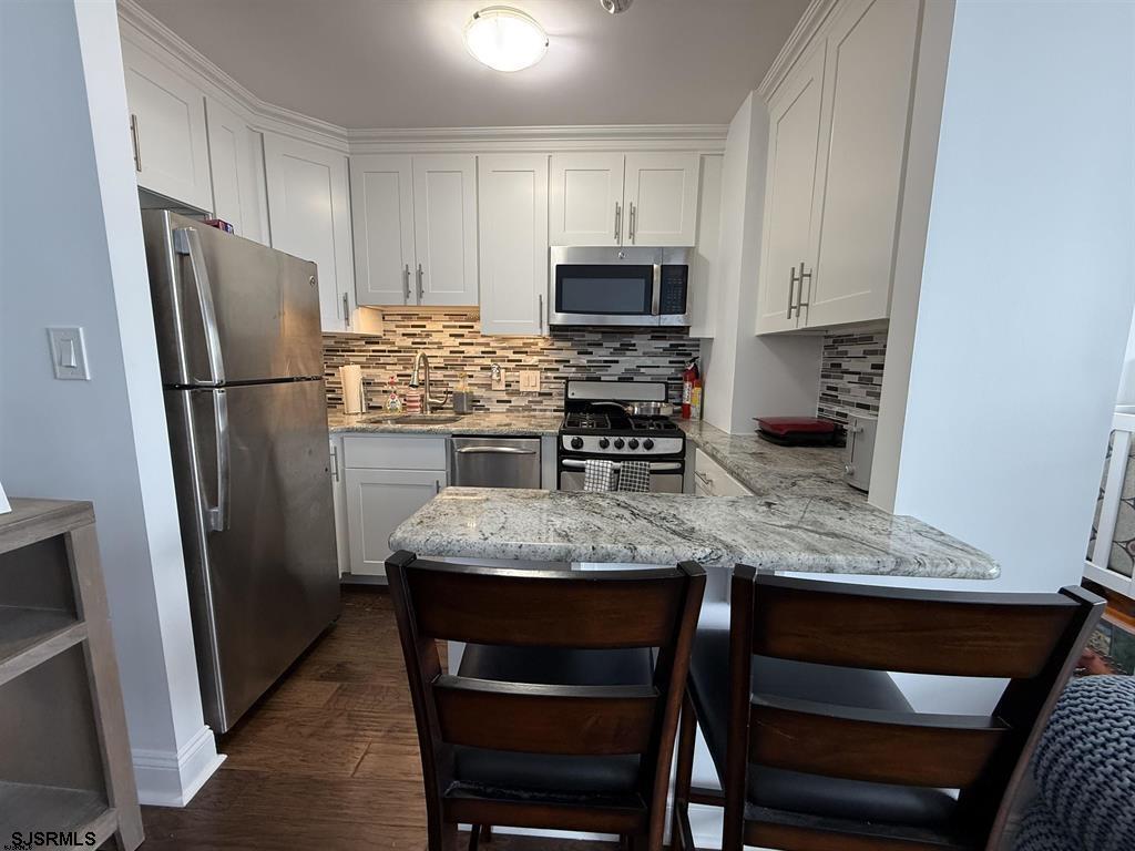 9400 Atlantic Avenue, Unit 306 Margate City, NJ 08402 - Photo 8 of 17 a kitchen with stainless steel appliances granite countertop a refrigerator a stove a sink dishwasher and white cabinets with wooden floor