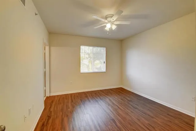 an empty room with wooden floor chandelier fan and windows