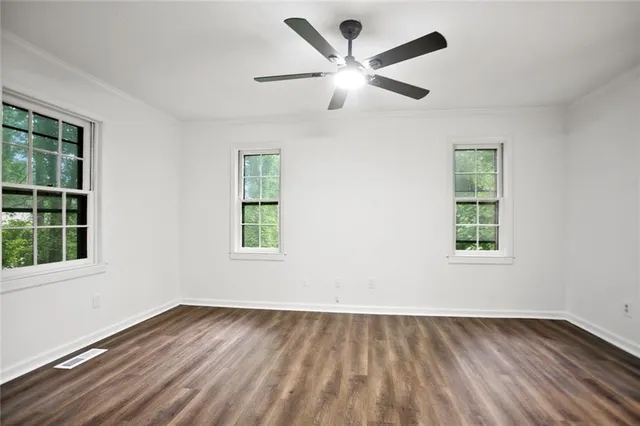 an empty room with wooden floor windows and fan