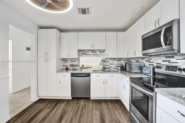 a kitchen with stainless steel appliances granite countertop a stove top oven a sink dishwasher and a refrigerator with wooden floor