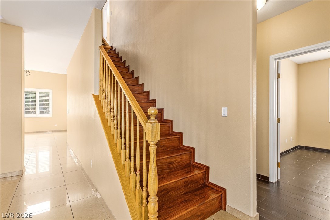 1477 Rancho Ridge Drive Henderson, NV 89012 - Photo 5 of 46 Elegant hardwood stairs with a matching banister ascend from a tiled entryway.