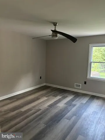 an empty room with wooden floor ceiling fan and window