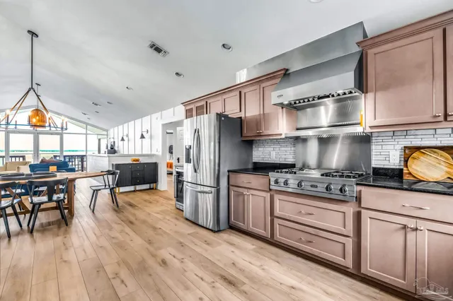 a kitchen with stainless steel appliances granite countertop a stove a refrigerator a kitchen island a dining table and chairs with wooden floor