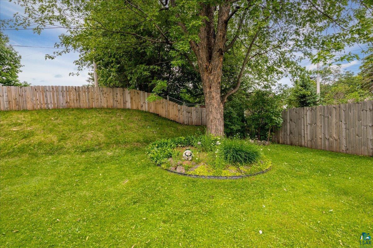 130 West Austin Street Duluth, MN 55803 - Photo 30 of 35 Expansive green lawn with a mature tree, featuring a defined garden bed with decorative rocks